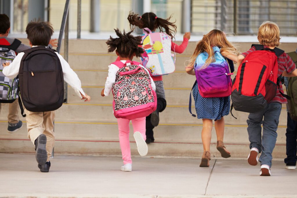 Group of children wearing backpacks, running up school steps together.