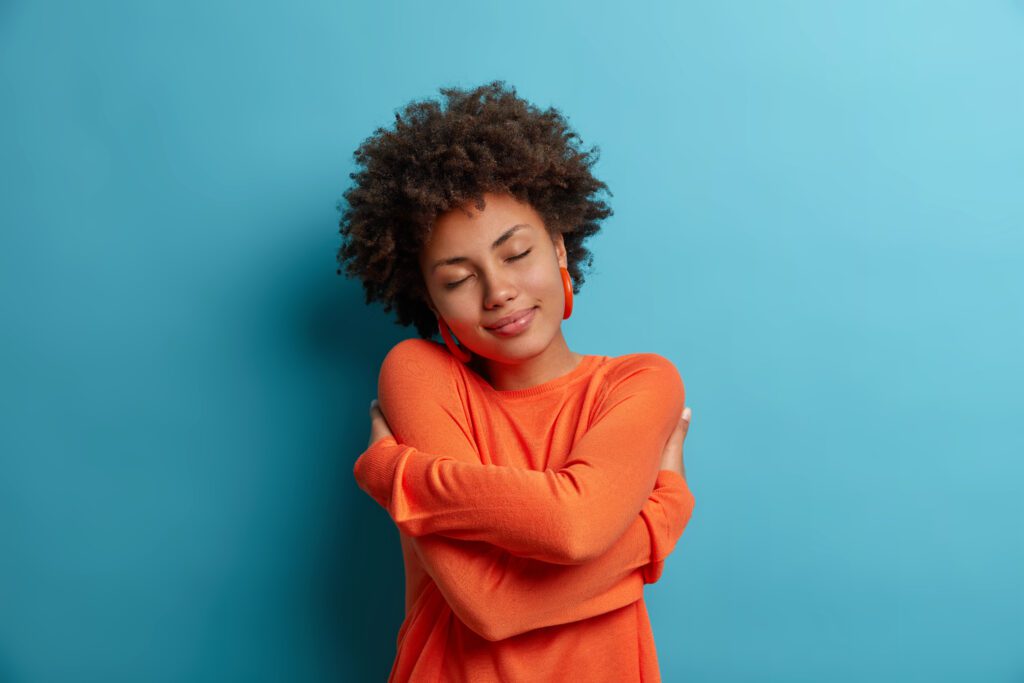 Smiling woman practicing self-love and self-care by hugging herself.