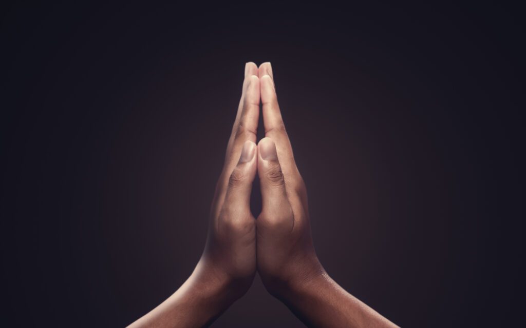 Close-up of two hands pressed together in a prayer gesture against a dark background.