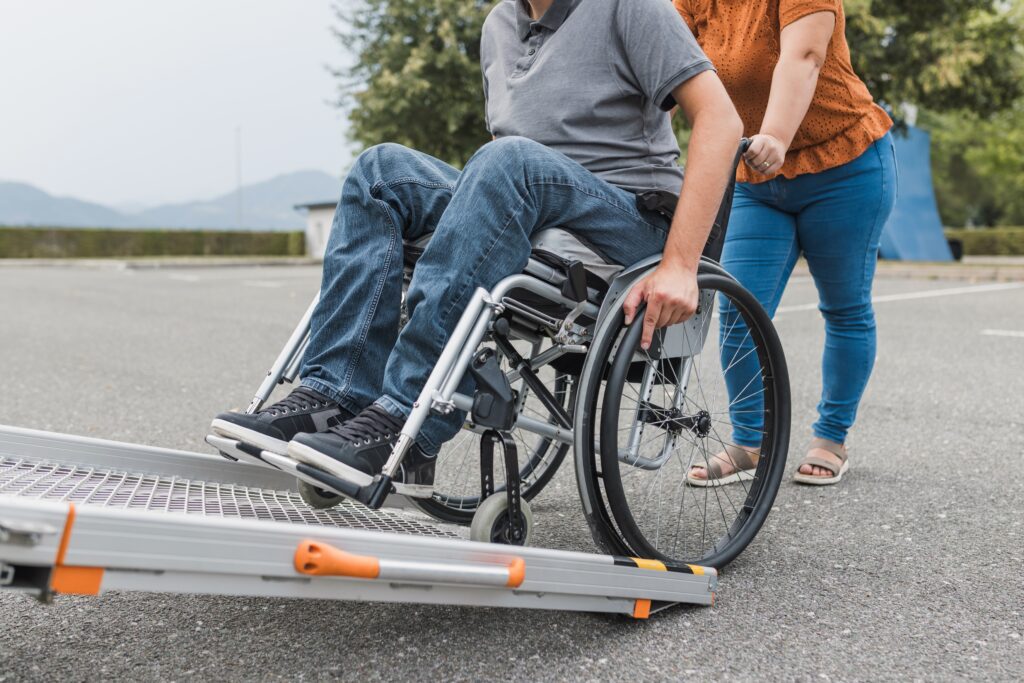 Wheelchair user with caregiver helping navigate a ramp, highlighting accessibility and support.