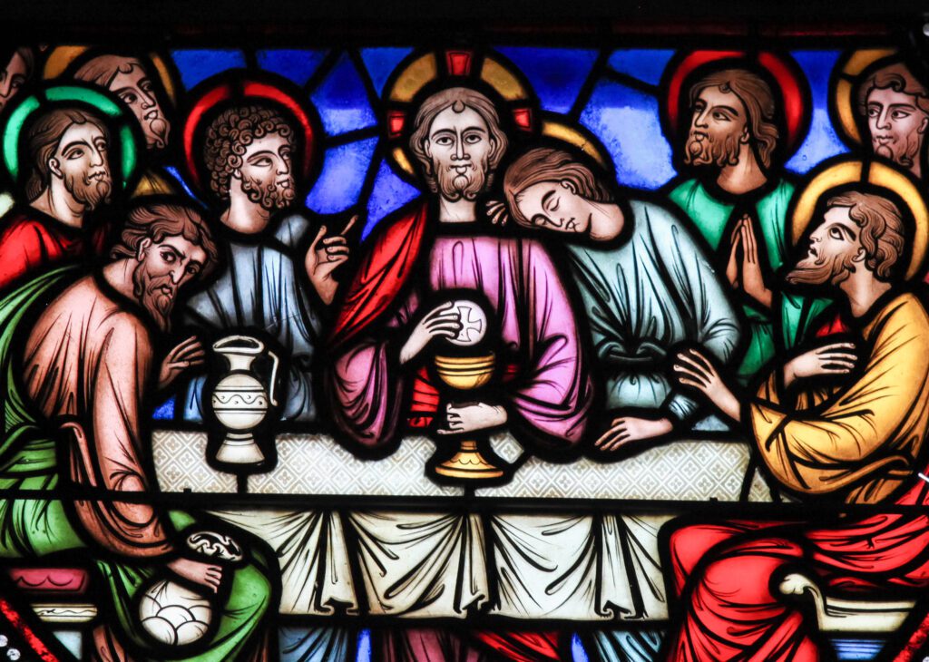 Stained glass window of Jesus and the apostles at the Last Supper, sharing bread and wine.