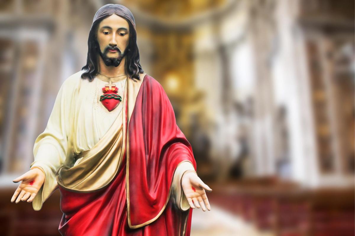 Statue of Jesus Christ with a red sash and open arms.