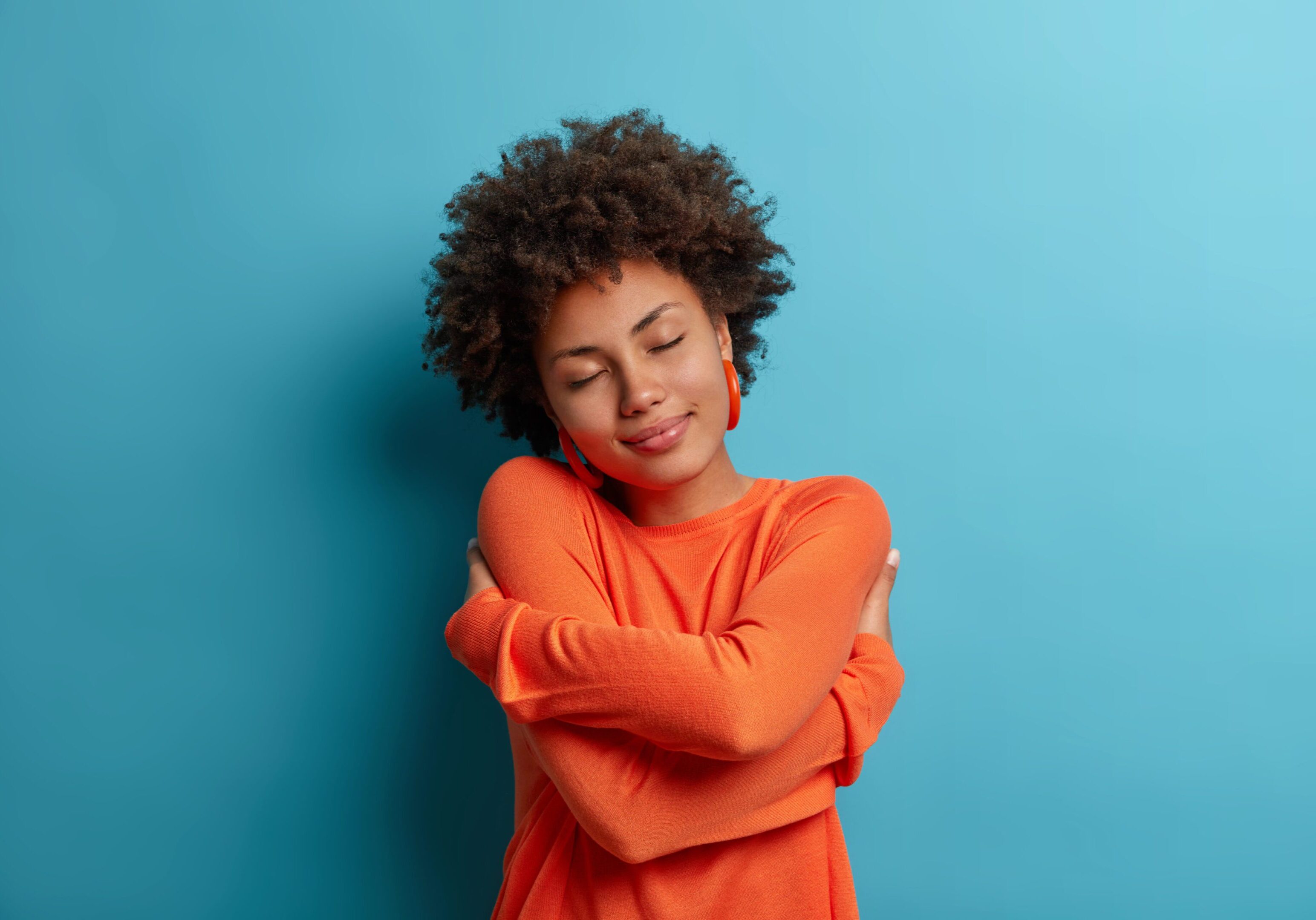 Smiling woman practicing self-love and self-care by hugging herself.