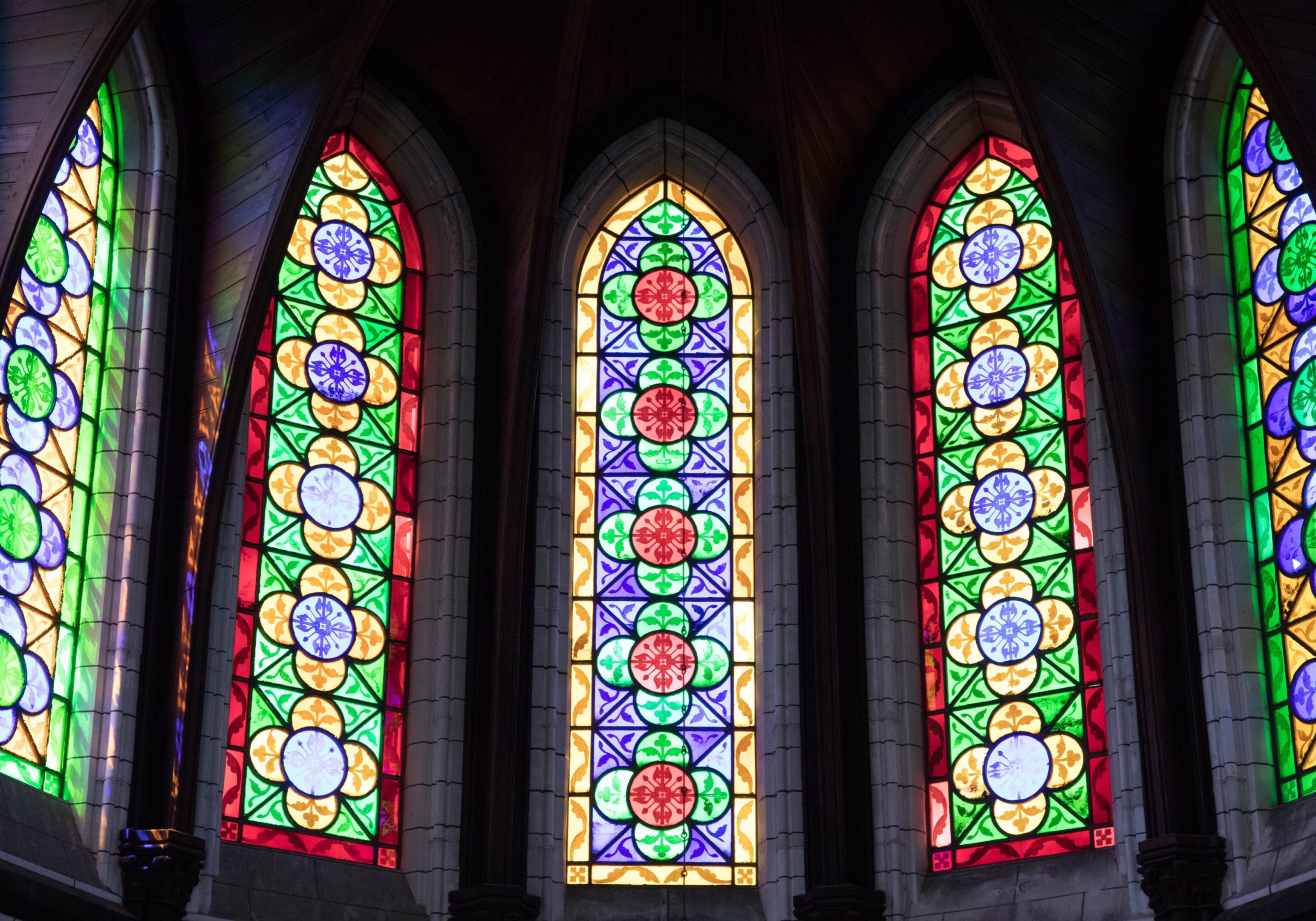 Gothic-style stained glass windows with vibrant floral and geometric designs in a cathedral.