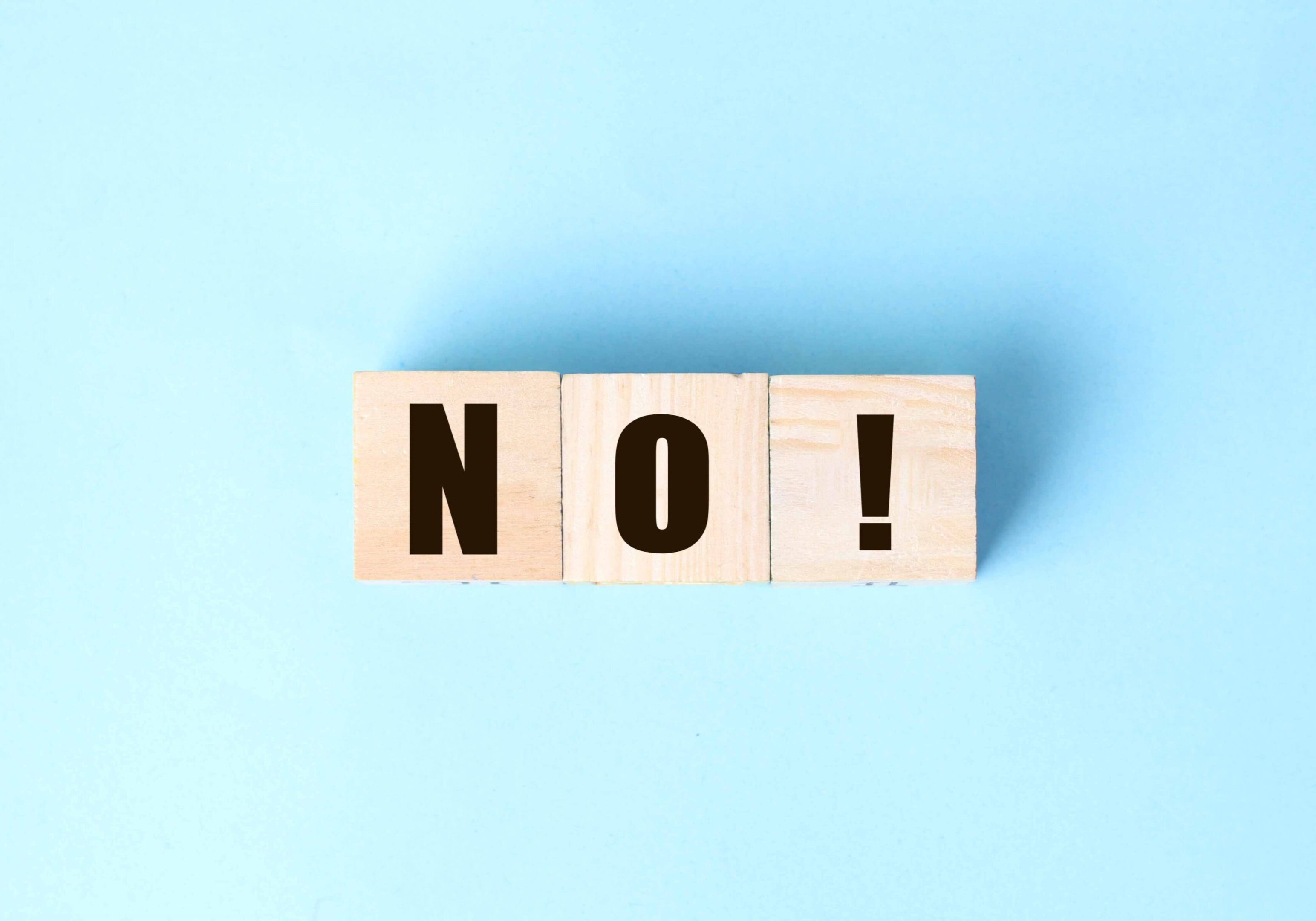 Wooden blocks spelling the word NO! on a light blue background.