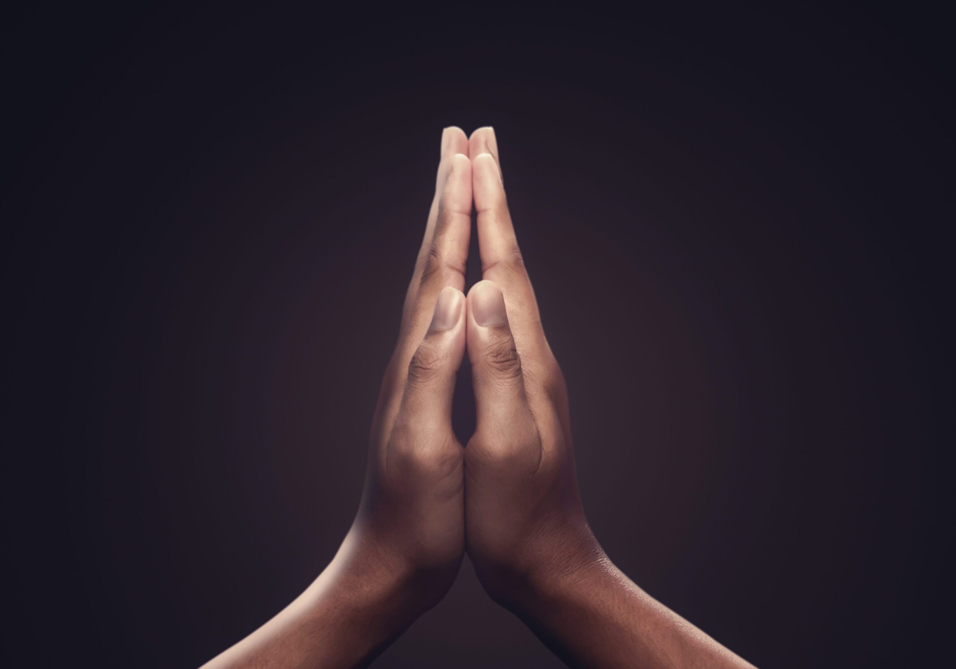 Close-up of two hands pressed together in a prayer gesture against a dark background.