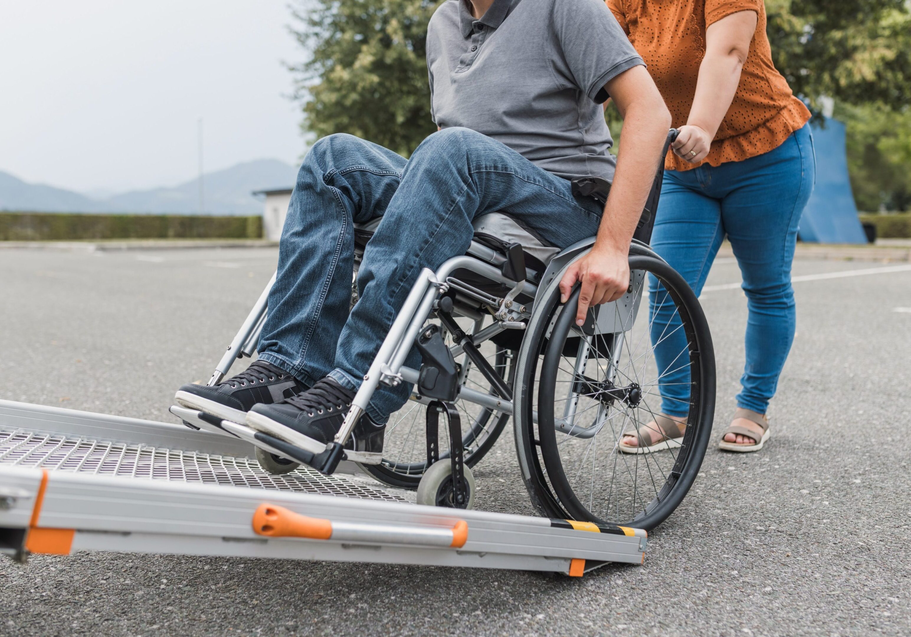 Wheelchair user with caregiver helping navigate a ramp, highlighting accessibility and support.