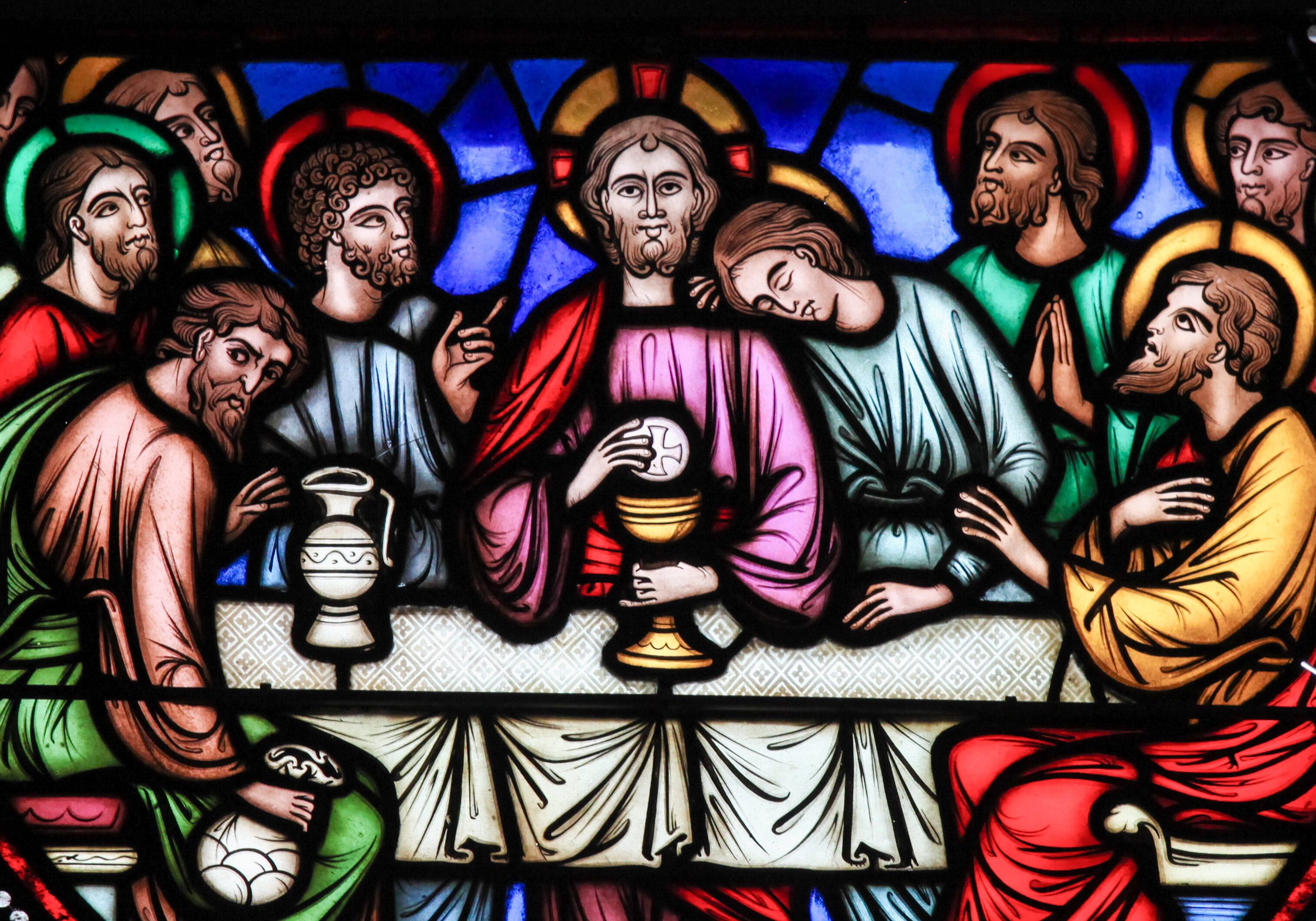 Stained glass window of Jesus and the apostles at the Last Supper, sharing bread and wine.